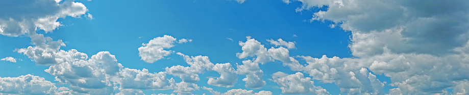 Blue sky with fluffy clouds wide background. Panoramic summer banner with bright sky and white clouds