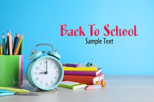 Alarm clock and different school stationery on white wooden table against light blue background. Mockup for design