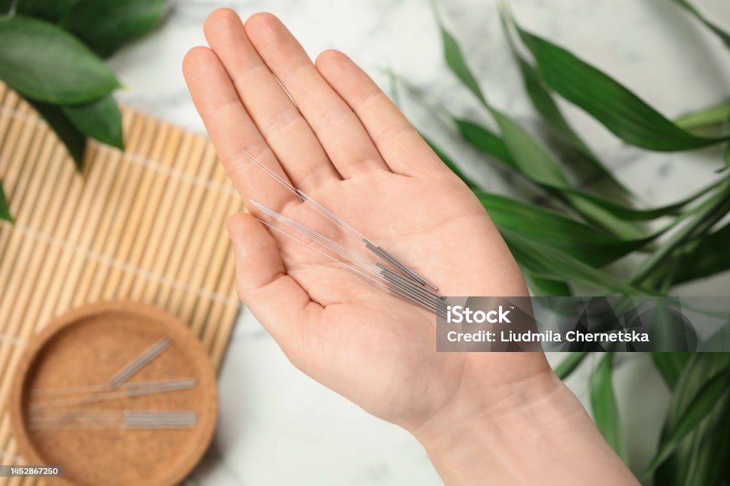 Woman holding many acupuncture needles over table, top view Acupuncture Stock Photo