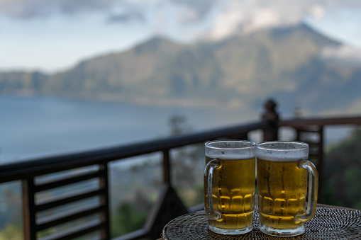 Panoramic view of a lake surrounded by mountain, tropical landscape with colourful clouds in the sky. Beer and food on table with view.