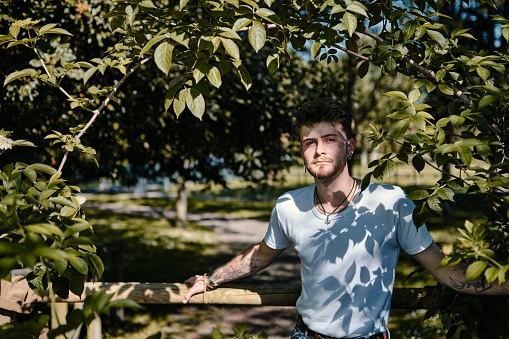 Man leaning back against a tree wearing jeans and a grey shirt, a sunny summer day.