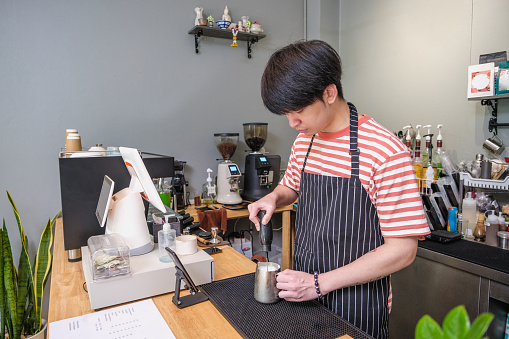 Young Asian Barista or coffee shop owner making a cup of coffee in bar counter at cafe, Small business owner concept