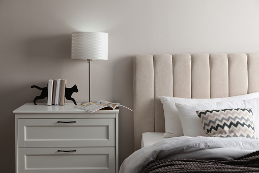 Stylish lamp, books and magazine on bedside table indoors. Bedroom interior elements