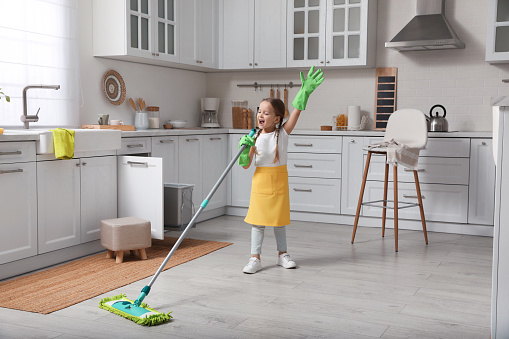 Cute little girl with mop singing while cleaning at home