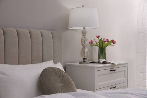 istock Stylish lamp, flowers and magazine on bedside table indoors. Bedroom interior elements 1452869455