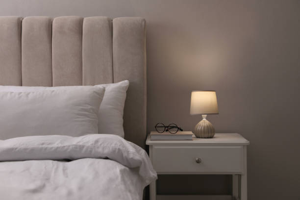 istock Stylish lamp, book and glasses on bedside table indoors. Bedroom interior elements 1452870613