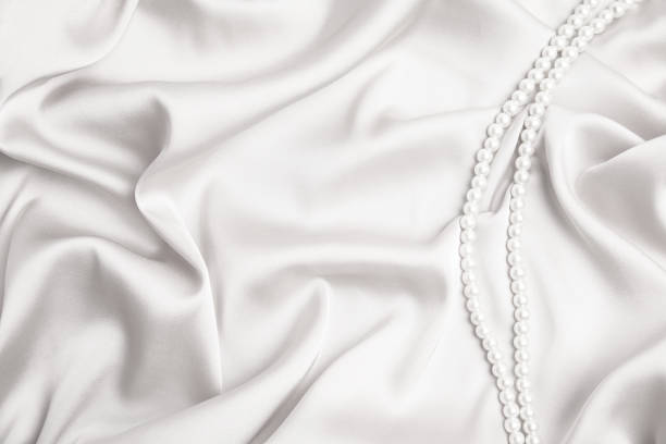 Beautiful pearls on white silk, top view