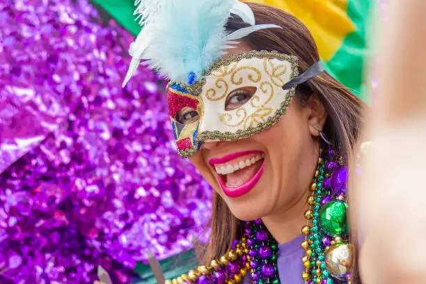 A young latin tourist female, wearing mask, costumes and necklaces celebrating Mardi Gras through the streets while taking a selfie with her cellphone in New Orleans. This is the most important celebration for the city.