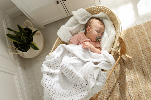 Cute little baby with pacifier sleeping in wicker crib at home, top view