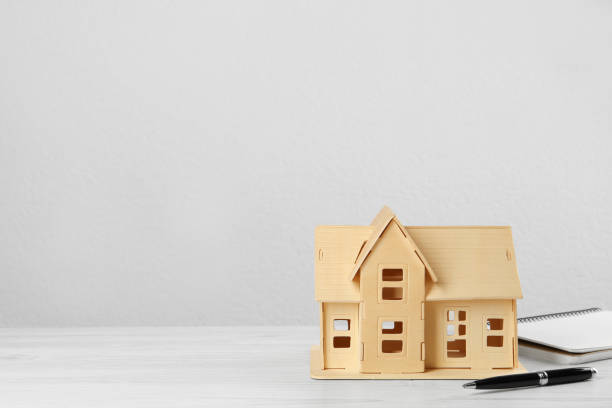 istock Mortgage concept. House model, notebook and pen on white wooden table, space for text 1452873240
