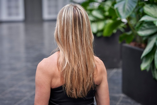 Yoga in room with green plants. Close-up rear view of blond woman with long hair