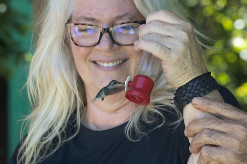 A smiling woman holding a feeder for a hummingbird