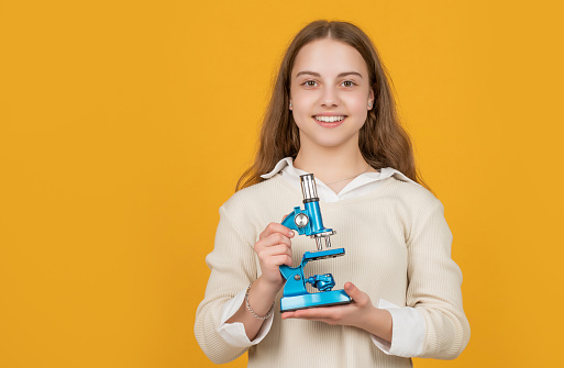 smiling child with microscope on yellow background.