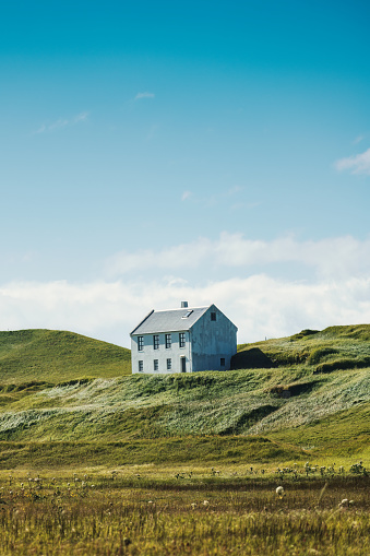 Lonely Nordic house on hill among the farmland in countryside on bright day at Iceland