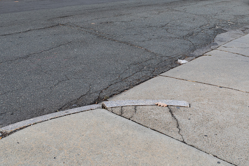 Cracked concrete driveway and curb leading into an asphalt street, transportation background, horizontal aspect