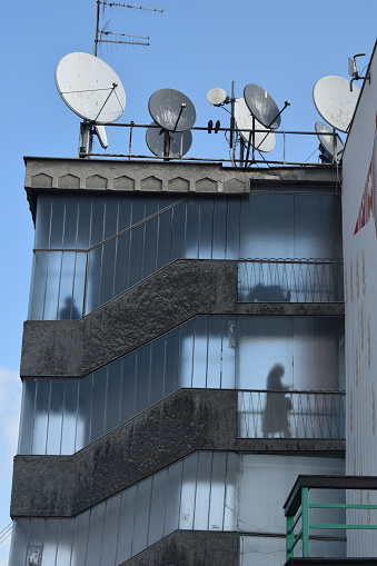 People standing inside of a transparent staircase of a building. Sunny day. Two birds and antennas on top of the building.