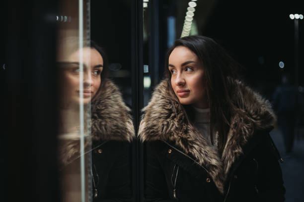 Beautiful young woman posing in front of shop window. Dressed well with make-up and nice winter jacket. Woman with long brown hair. Happiness and confident.Christmas and New Year vibes.