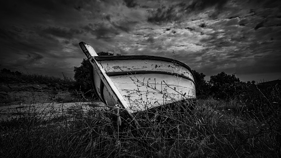 A grayscale low angle shot of an old wooden boat on a field