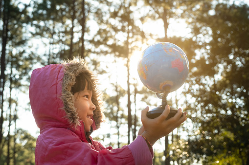 Cute Asian girl learning model of the world on nature background and warm sunlight in the park. Children learn through educational play activities. Earth day. World environment day.