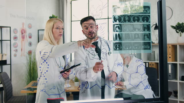 Attractive high-skilled successful male and female doctors working together in medical lab with patient's x-ray scan comparing with schematically depicted skeleton on glass wall
