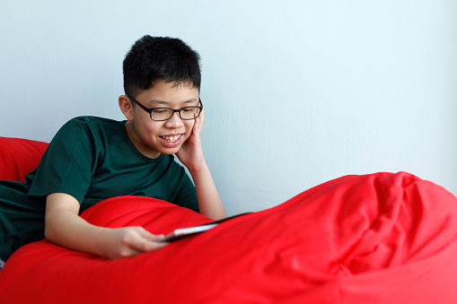 Asian boy reading book on a bean bag. Children leisure reading concept