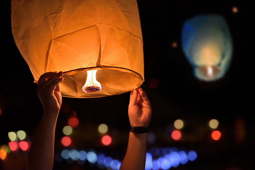 Young man hands release sky lanterns on festival. Warm light from fire