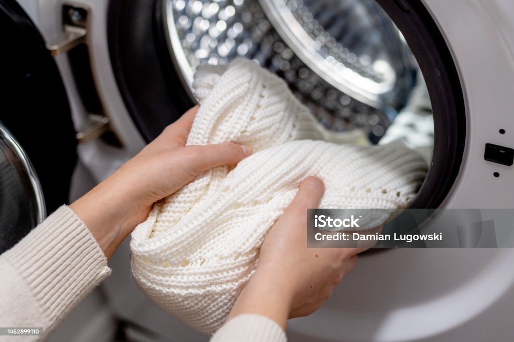 Woman putting white clothes into the drum of a washing machine, front view. Washing dirty clothes in the washer Laundry Stock Photo