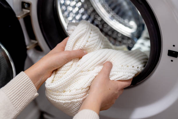 Woman putting white clothes into the drum of a washing machine, front view. Washing dirty clothes in the washer stock photo