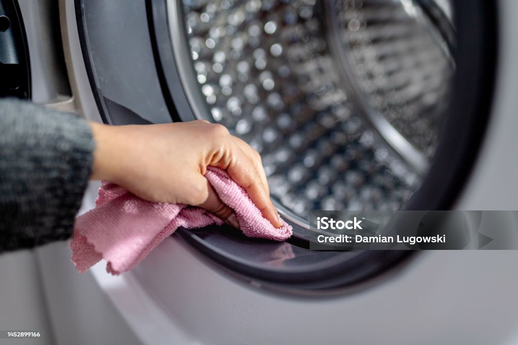 Female hand cleaning washing machine from dirt with pink cloth. Wiping rubber seal on washing machine drum Female hand cleaning washing machine from dirt with pink cloth. Wiping rubber seal on washing machine drum, close up Cleaning Stock Photo