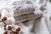 Stack of clean white towels and cotton branch with fluffy cotton bolls on soft blanket. Folding laundry and towels