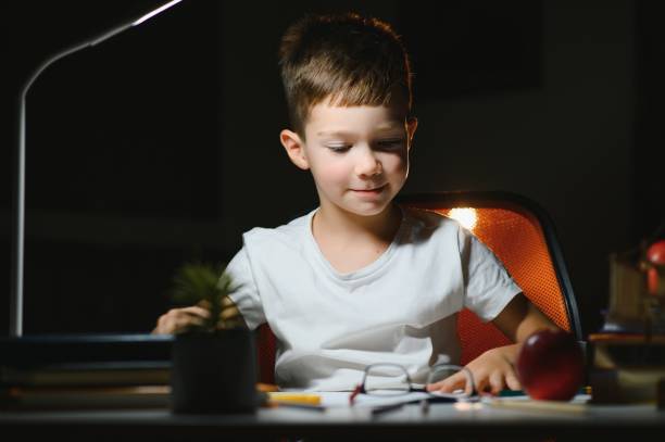 istock Boy learn lessons in the home setting at the table in the light of a table lamp. 1452900603