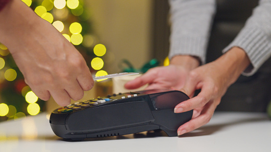 Closeup hand of asian woman purchase by credit card on electronic payment machine or card reader in small shop at christmas night. Celebrate christmas and new year holidays concept.