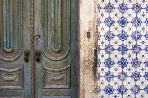 Brass hand shaped door knockers on an old and weathered door. The wall is covered with blue and white Portugese azulejos.