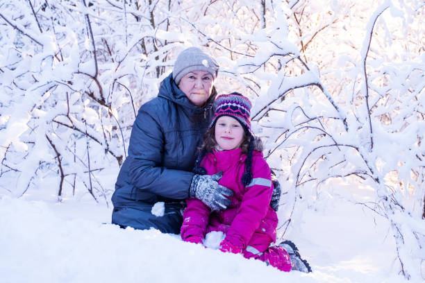portrét. starší žena ve věku 77 let, dívka ve věku 7 let se usmívají a dívají se do kamery na pozadí sněhem pokrytých větví stromů a slunečního světla. - deep snow fotky - stock snímky, obrázky a fotky
