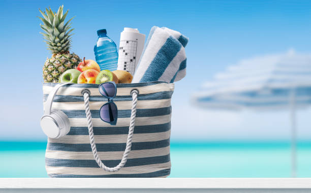 Beach bag with accessories and tropical beach Stylish beach bag with accessories and tropical beach in the background, summer vacations concept beach bag stock pictures, royalty-free photos & images
