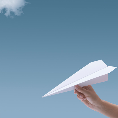 Woman holding a paper airplane and blue sky in the background, creativity and imagination concept, blank copy space