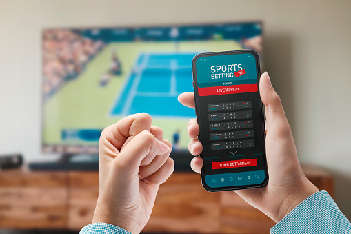Live in-play betting app on smartphone display, a woman is betting at home and winning, POV shot
