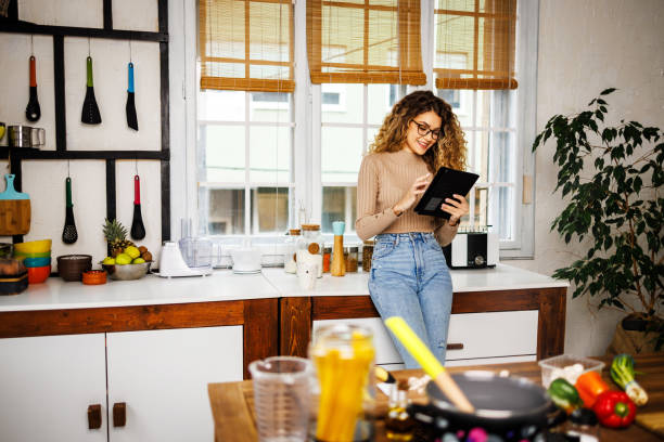 istock Smiling young woman reading on digital tablet in the kitchen 1452910328