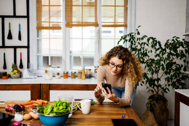 istock Smiling woman using smartphone in the kitchen 1452910965