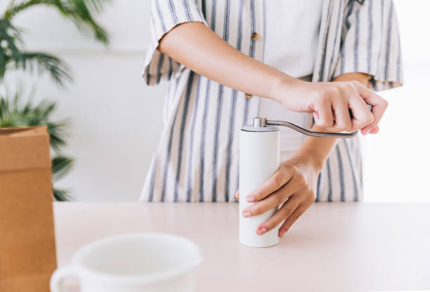 istock Crop woman hand using white color hand coffee grinders on the table before making pour-over on ground coffee over the paper filter on a glass dripper. An alternative method is called Dripping. 1452912286