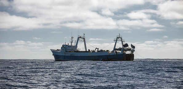 Large fishing trawler conducts industrial fishing in the open ocean. Old fishing vessel on the horizon is operating in southern oceanic waters.