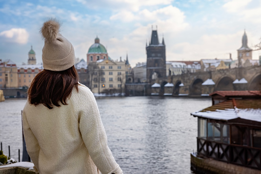 A tourist woman in winter clothing enjoys the view of the snow covered skyline of Prague with Charles Bridge and old town