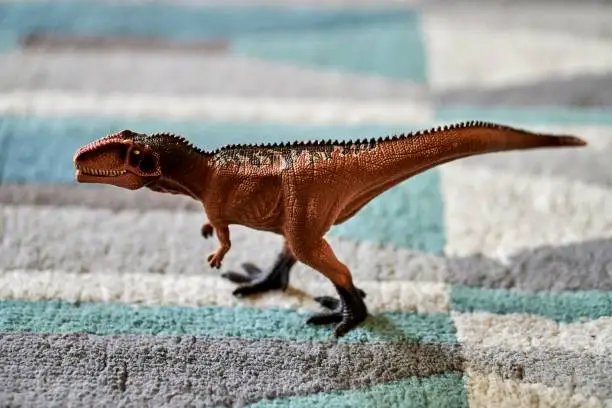 A closeup shot of a giganotosaurus dinosaur toy figurine on a carpet floor with blurred background