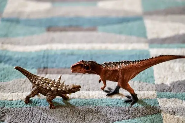 A closeup shot of the Animantarx and Giganotosaurus dinosaurs toy figurines on a carpet floor with a blurred background