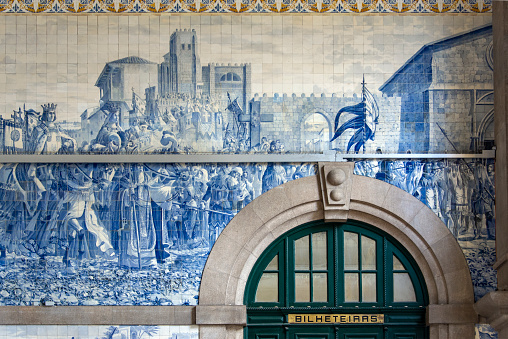 Walls covered with azulejos in the São Bento railway station in Porto. The direction for tickets bilheteiras on a brass plate above the door.