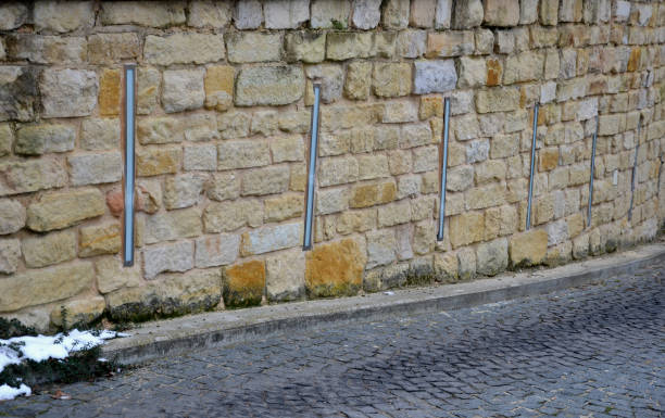 beautifully folded retaining wall with granite attic with small joints. brown beige yellow irregular gneiss holding slope above it. long vertically placed lights inside the wall. entrance to garage, patio garden. irregular