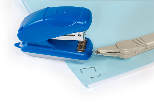 Small manual paper stapler and simple pen type staple remover on stapled paper sheets on a white background