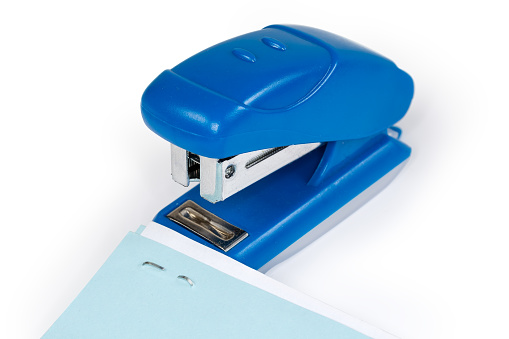 Small manual paper stapler with stapled blue and white sheets on a foreground, close-up in selective focus