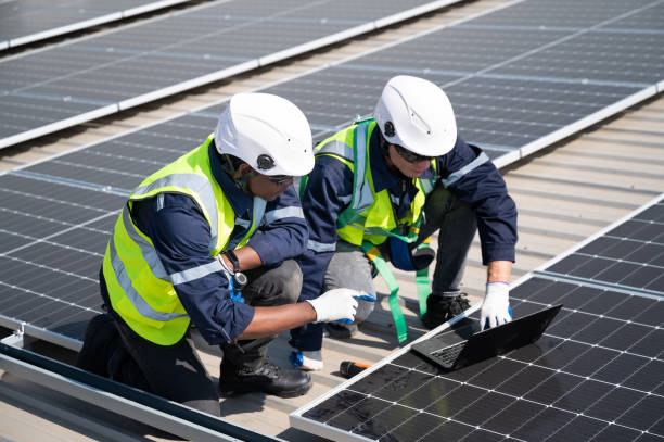 istock Caucasian and African American engineer man use electric screwdriver and computer notebook working with solar panel on roof factory 1452924261