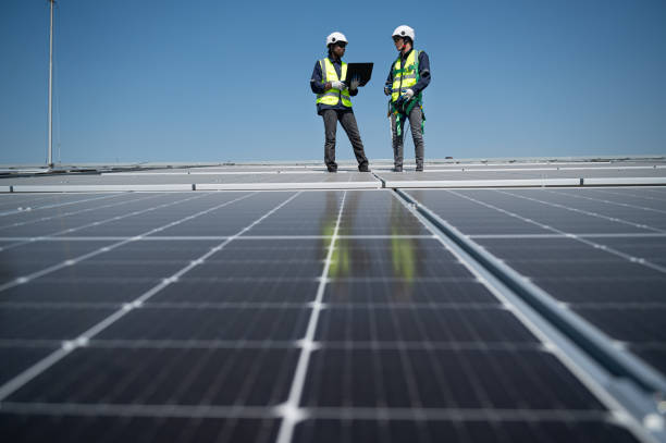istock Caucasian and African American engineer man use electric screwdriver and computer notebook working with solar panel on roof factory 1452924782
